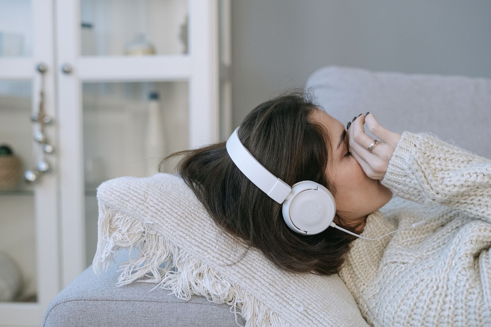A woman resting with headphones on, eyes closed, listening in the low light